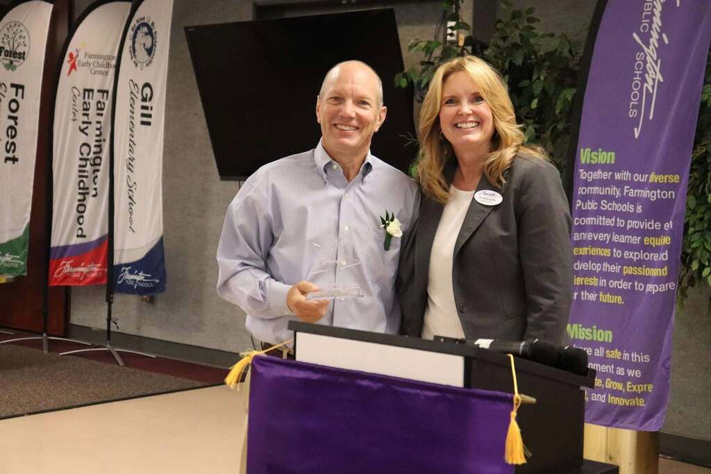 Two people standing behind a podium with banners for Farmington Public Schools and early childhood education in the background.
