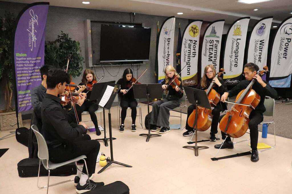 A group of young musicians playing string instruments in a circle during a rehearsal or performance indoors.