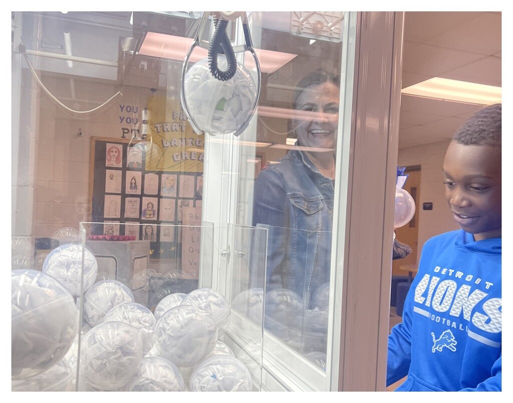 A student looking info the claw machine with an adult smiling near him