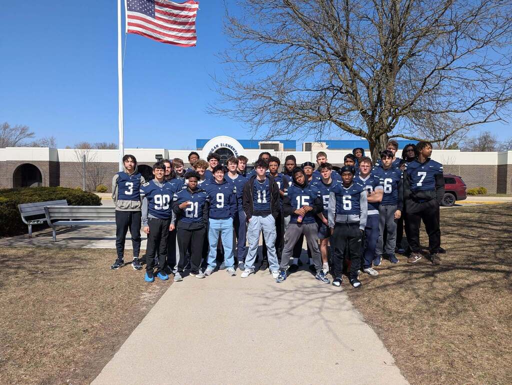 A large team of high school football players standing in front of Lanigan Elementary