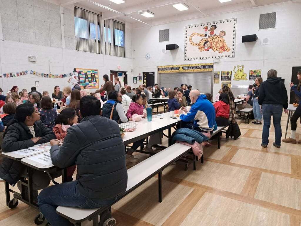 A wide shot of the cafeteria with students and their family members sitting at tables talking