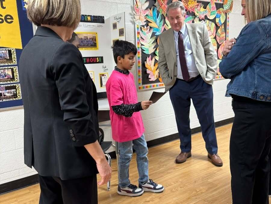 A Longacre student reading from a card, presenting to adult guests at the school