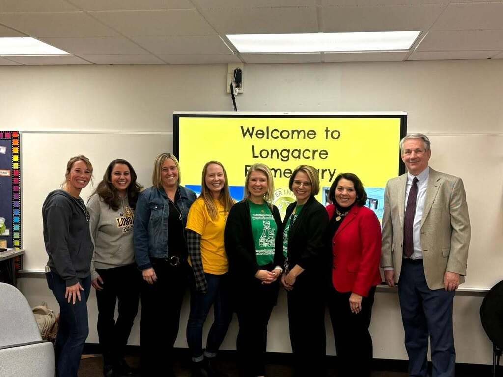 A group of adults standing in front of a sign that says Welcome to Longacre