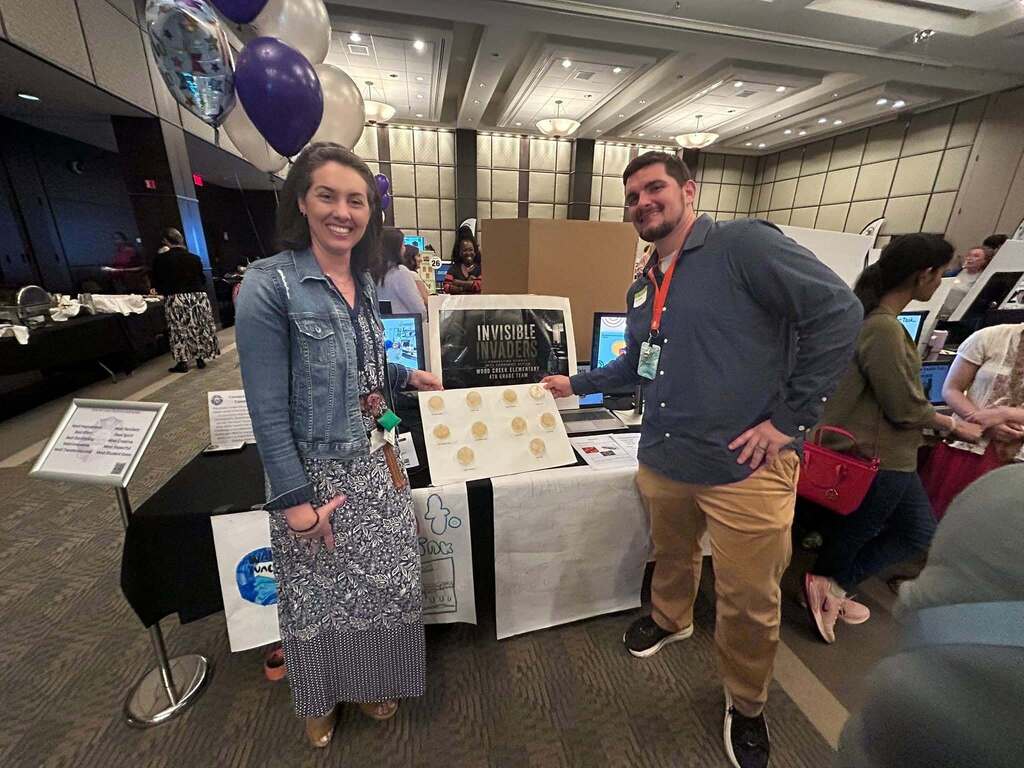 Two smiling adults next to a conference display