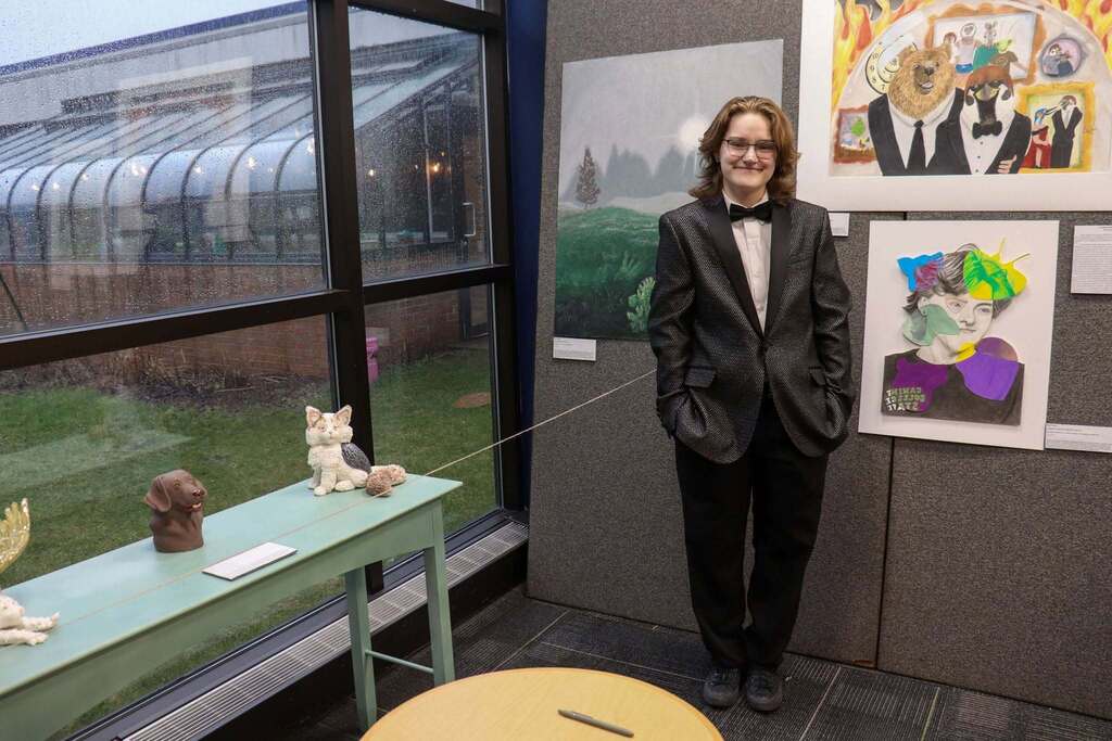 An IB student standing in front of artwork, smiling at the showcase event.