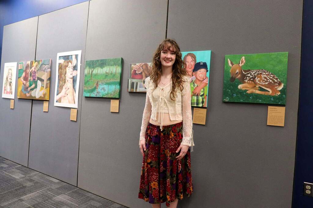 An IB student standing in front of art smiling at the camera