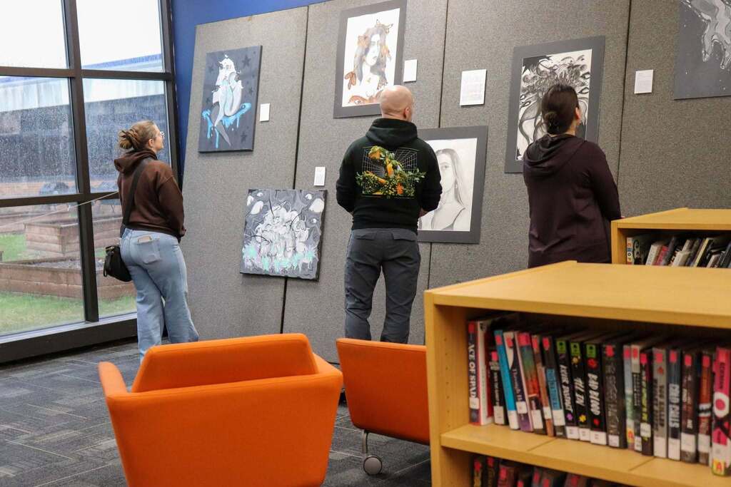 Three adults looking at various artwork pieces.