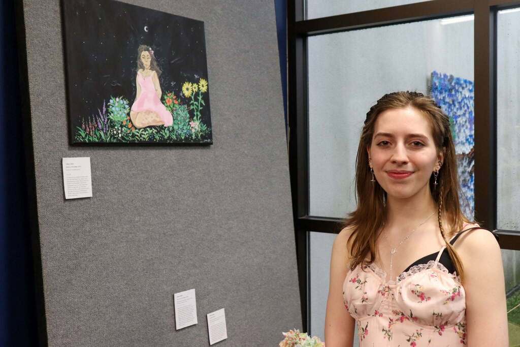 An IB student standing in front of her artwork and smiling.