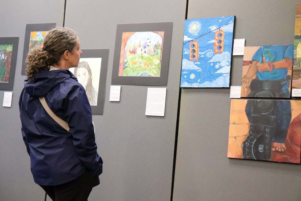 An adult looking at various pieces of art from the IB art showcase.