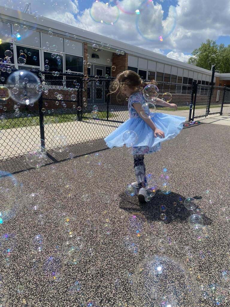 FECC student dances on the playground in a blue dress surrounded by bubbles floating in the air.