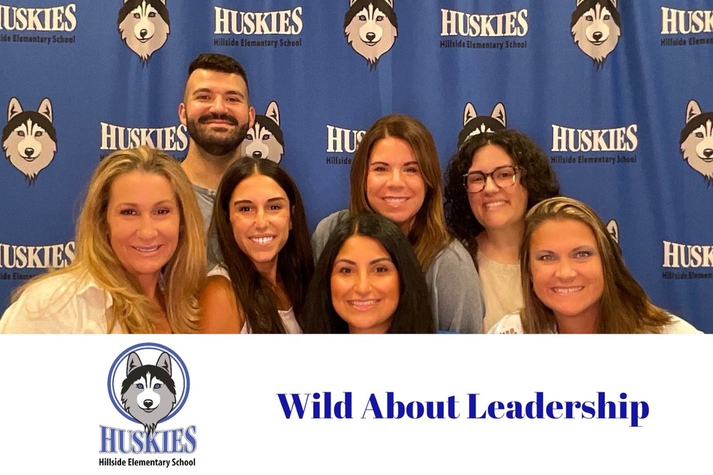 Seven smiling staff members pose in front of a Hillside Elementary School Huskies backdrop promoting leadership.