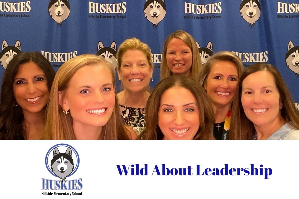 Seven smiling women posing in front of a blue backdrop with 'Huskies Hillside Elementary School' logos.
