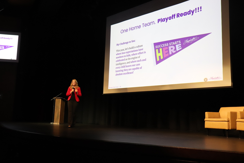 Speaker at podium addressing audience during Opening Day event with presentation slide showing a t-shirt and trophy graphic.