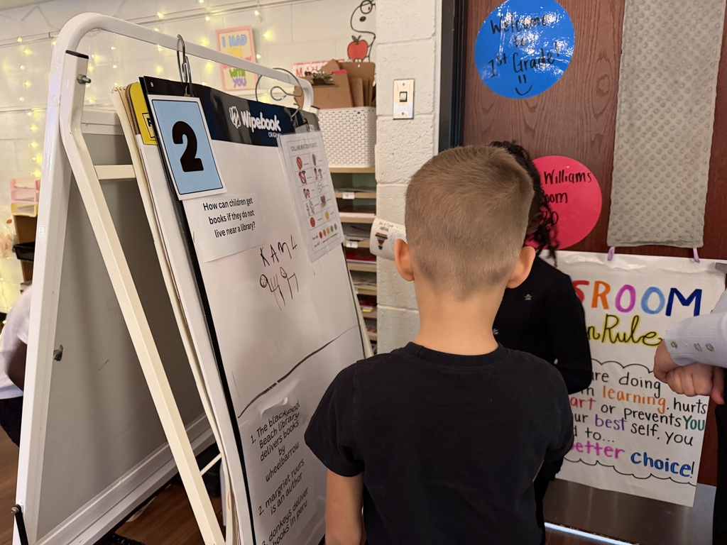 two young boys examining a whiteboard with drawings and educational text about how children get ideas for stories.