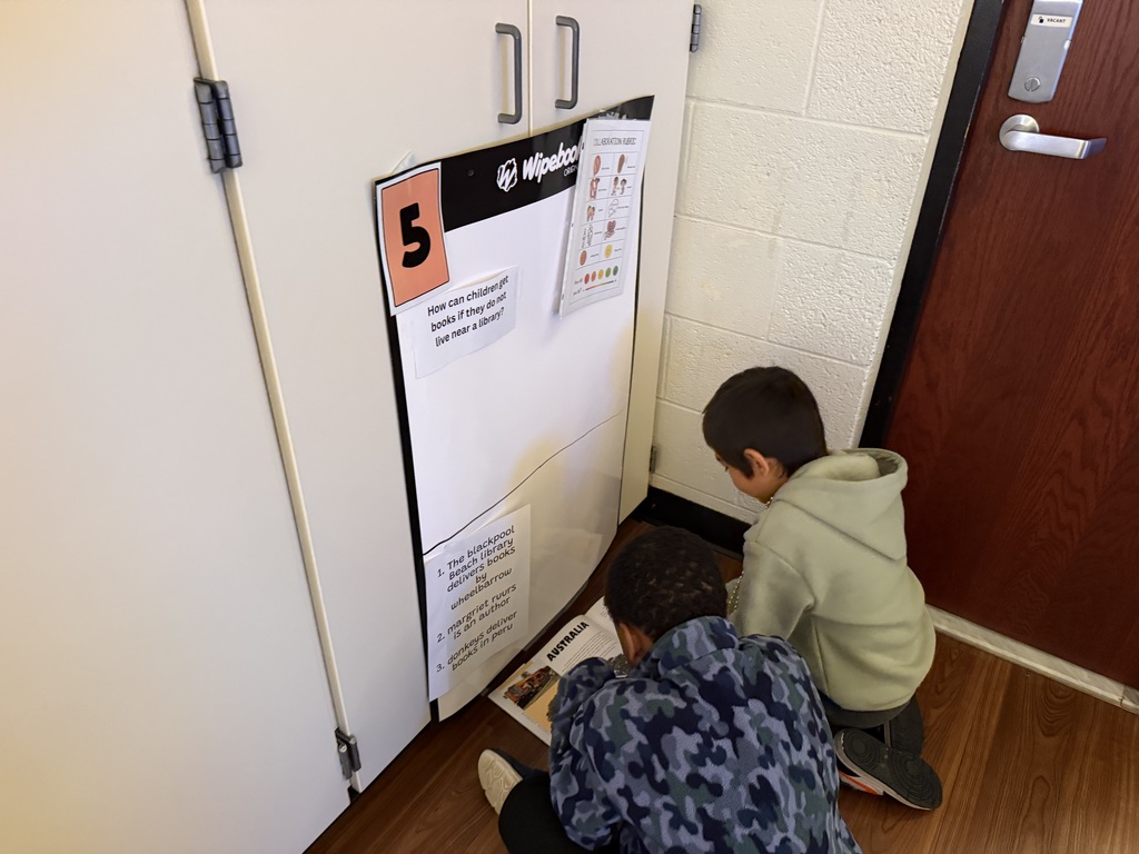 two young boys sitting on the floor examining a whiteboard with a prompt asking how children can get books if they don't live near a library