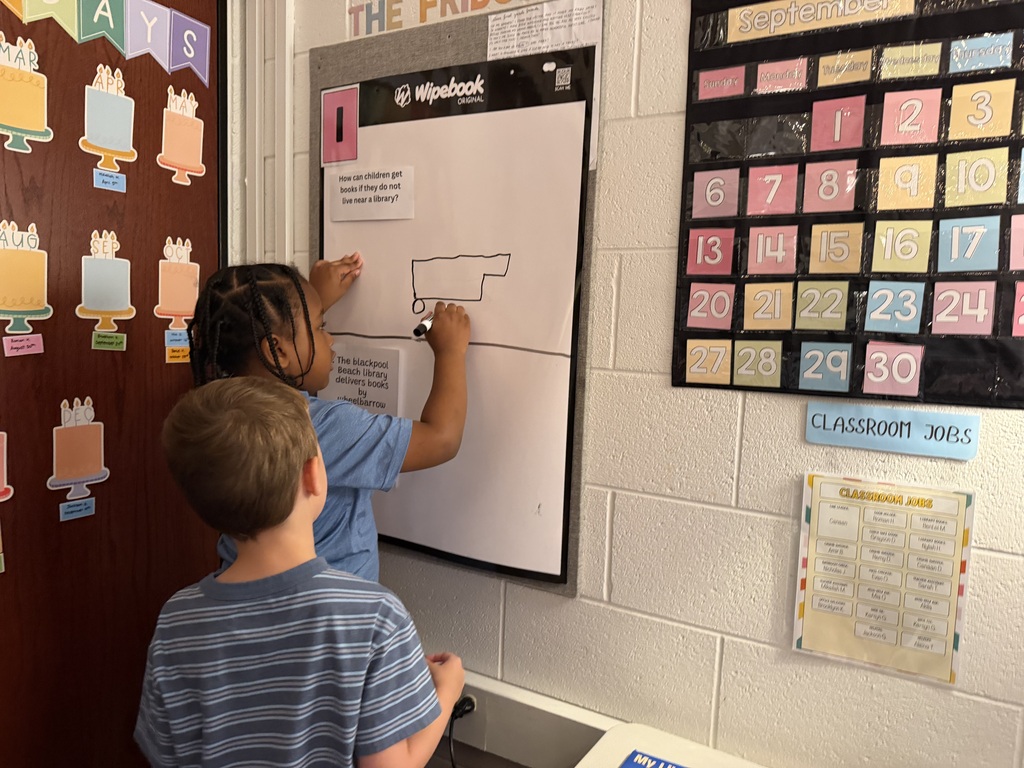 two young boys drawing a photo of a car on a pad of paper