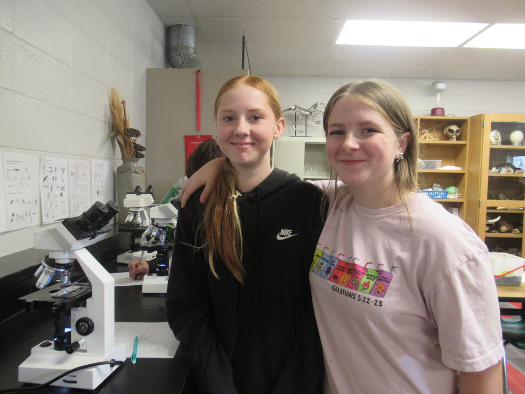 two girls smiling while looking into a micro scope