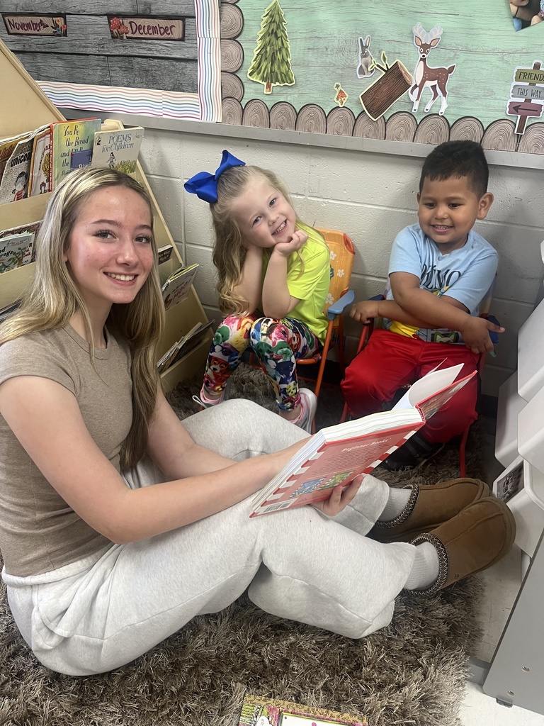 FJHS Student reads to PreK students, sitting on carpet
