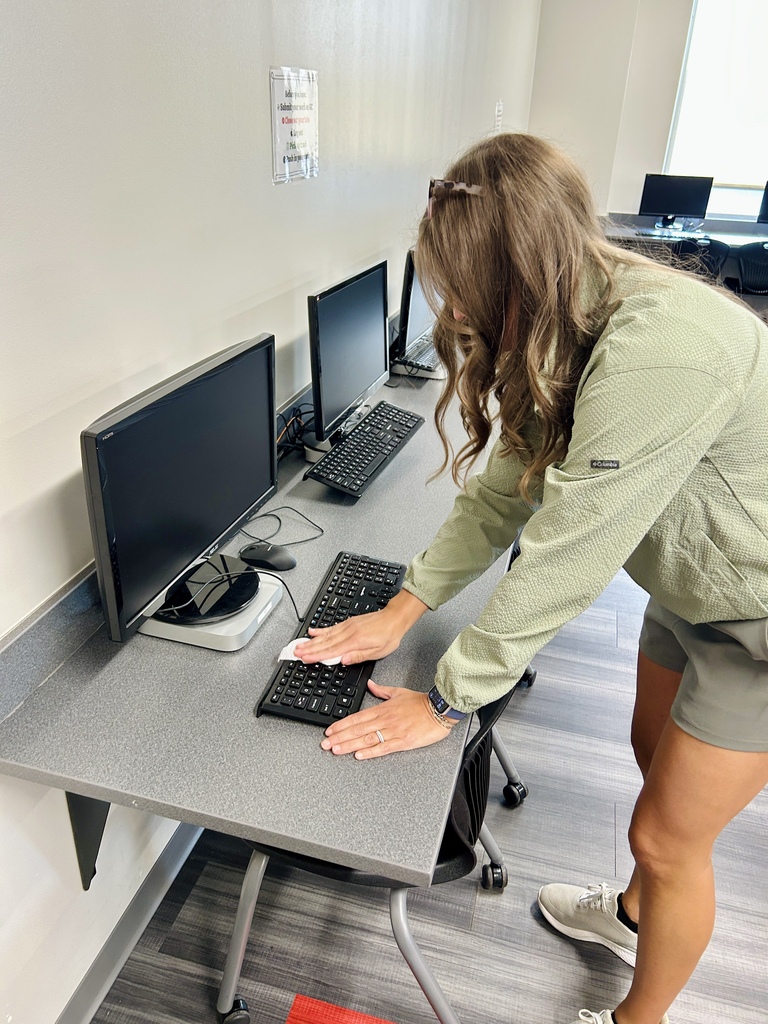Person in a green jacket working at a computer desk, with two computer monitors, keyboards, and mice.