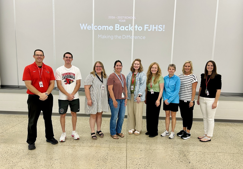 Nine adults stand in a row in front of a wall with a welcome sign.