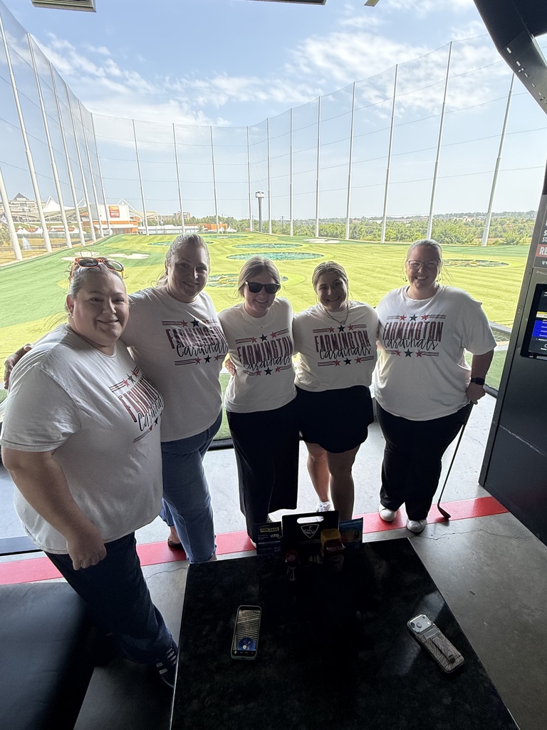 Five people in white shirts stand in front of a golf driving range with a grassy field in the distance.