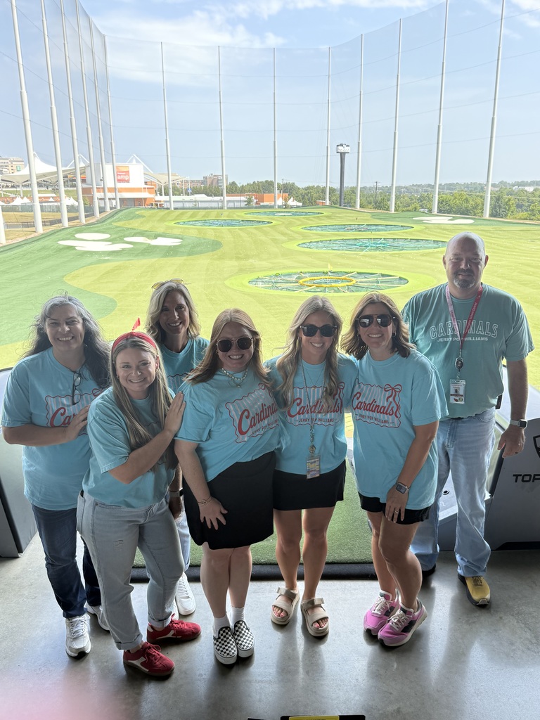 Group of people in matching shirts at a golf driving range with a green field in the background.