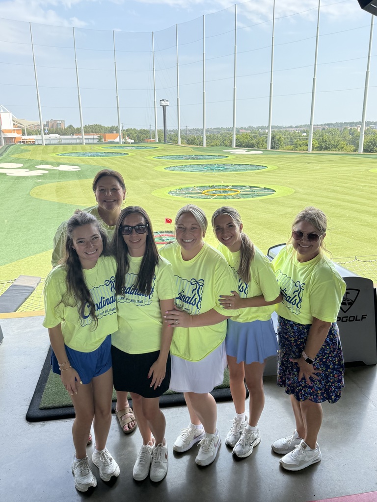 A group of women in yellow shirts and white shoes standing together, with a golf course in the background.