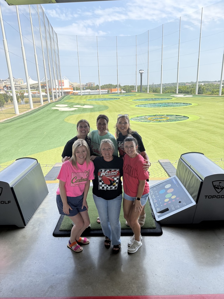 Six people stand in a golf driving range, smiling. Behind them is a large window with a view of a golf course.
