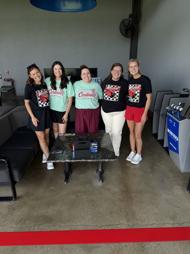 Five women in matching shirts stand around a table in an indoor area with gray walls and a red line.