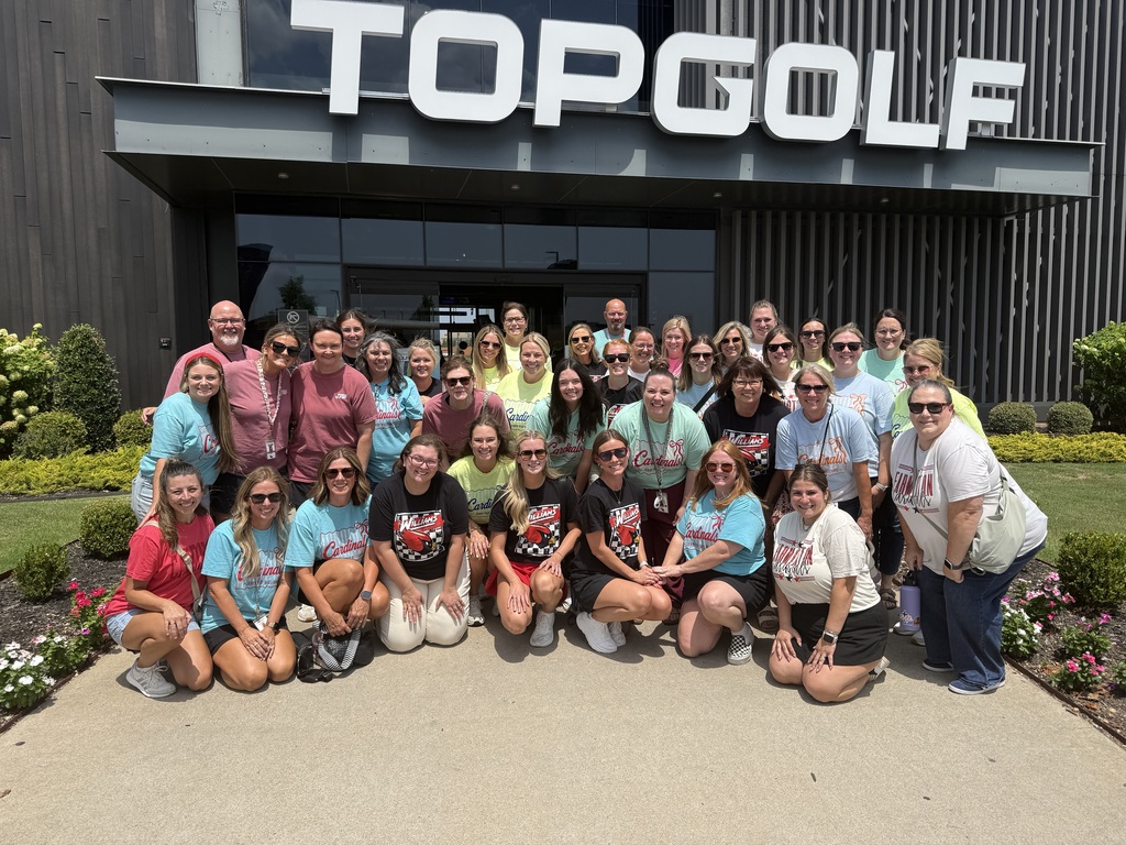 A group of people wearing various shirts poses for a photo in front of the Top Golf building.