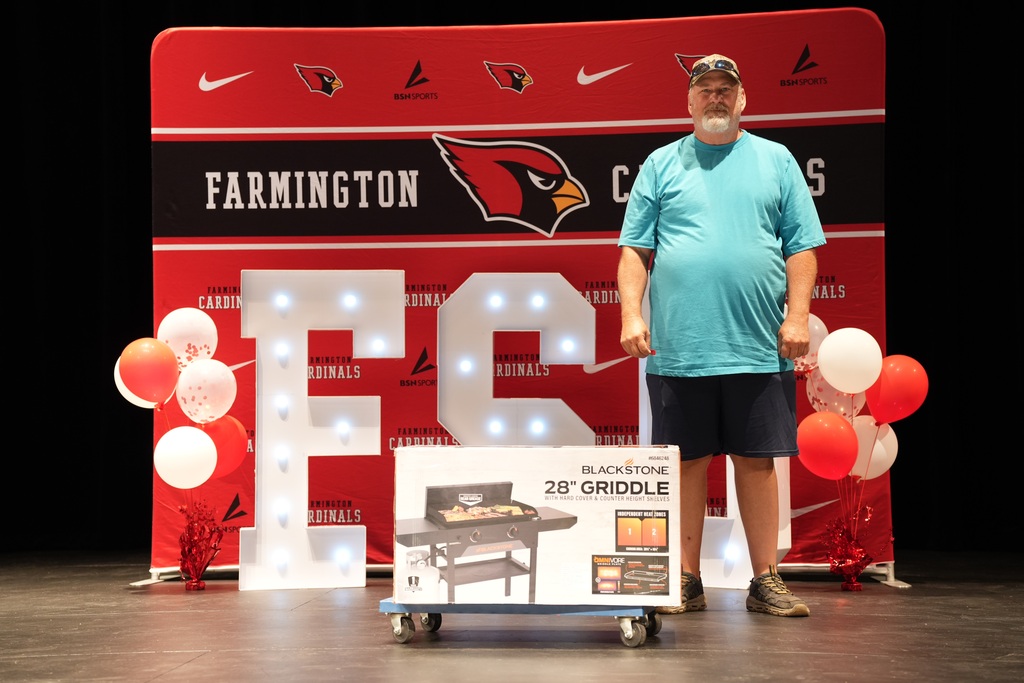 A man in a light blue shirt stands on a stage with a grill, balloons, and a large "EC" sign.