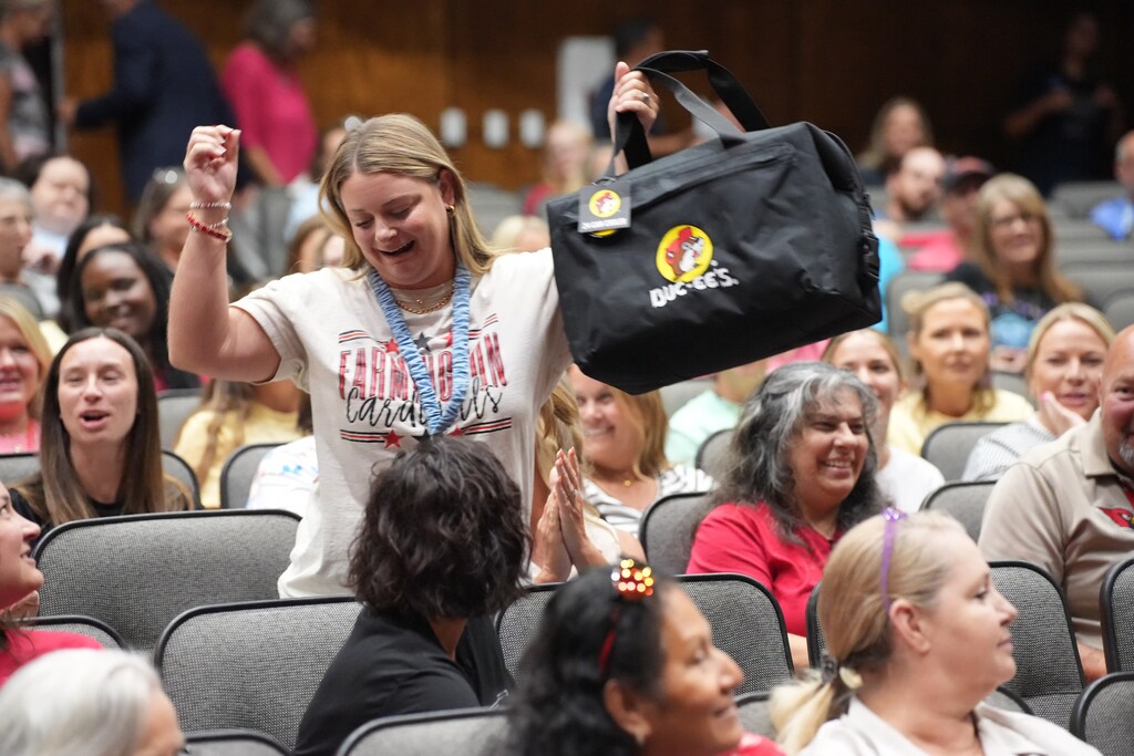 Woman holds a black bag up in the air as a crowd of people claps and cheers.