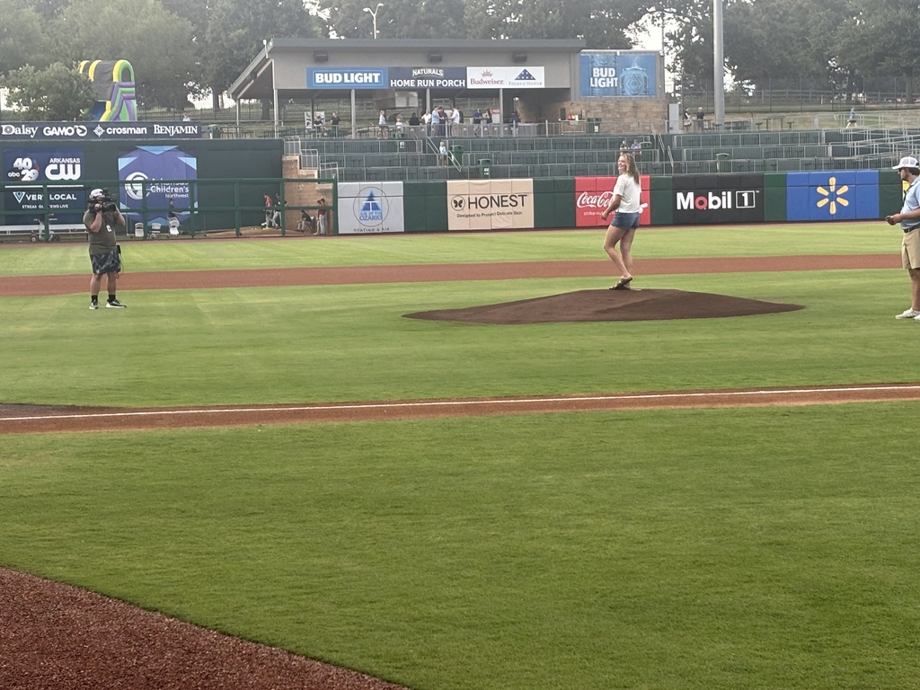 A baseball field with people standing on the pitcher's mound and others standing on the sidelines.