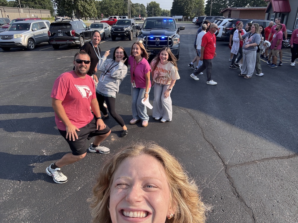 Group of people smiling and posing for a photo in a parking lot with several vehicles.