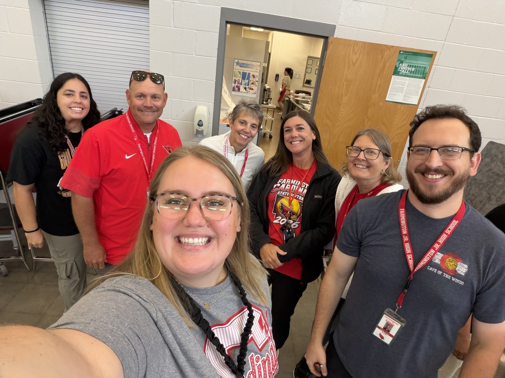 A group of people in an indoor area, smiling and standing together. Most wear red shirts, while some have glasses.