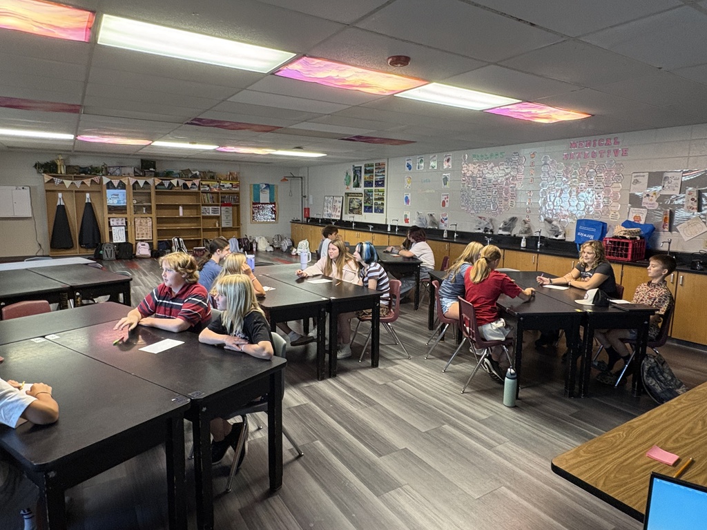 An indoor classroom with wood floors and tables. A group of people sit at tables.