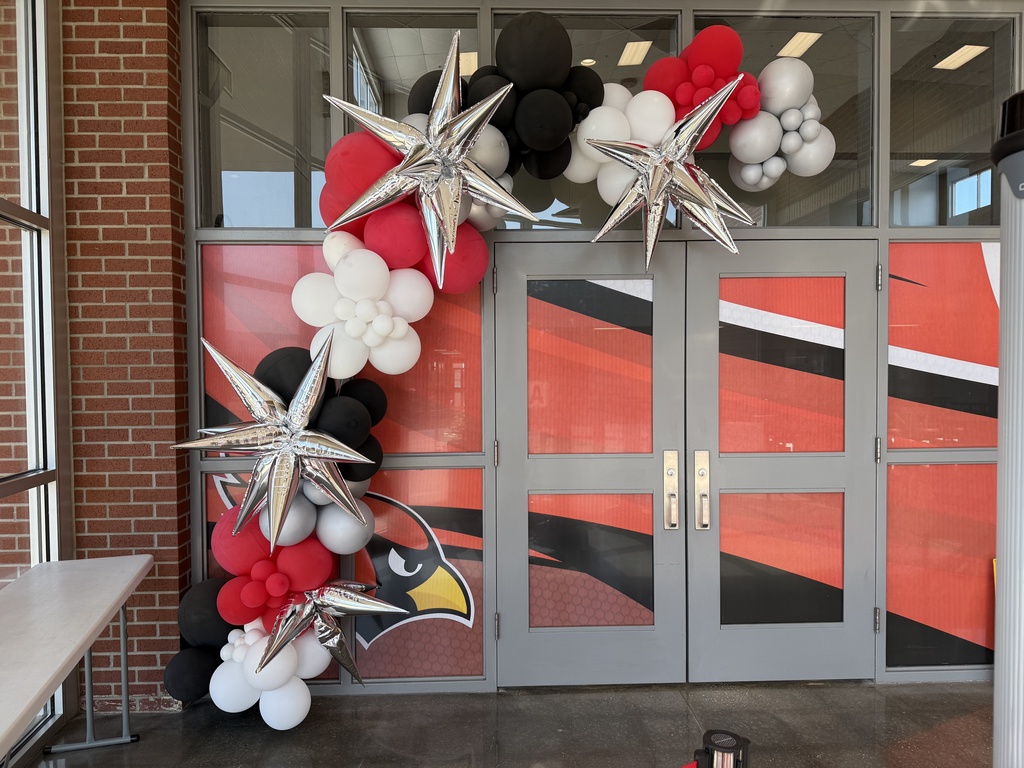 A decorated arch of red, white, black, and silver balloons outside a building with a brick wall.