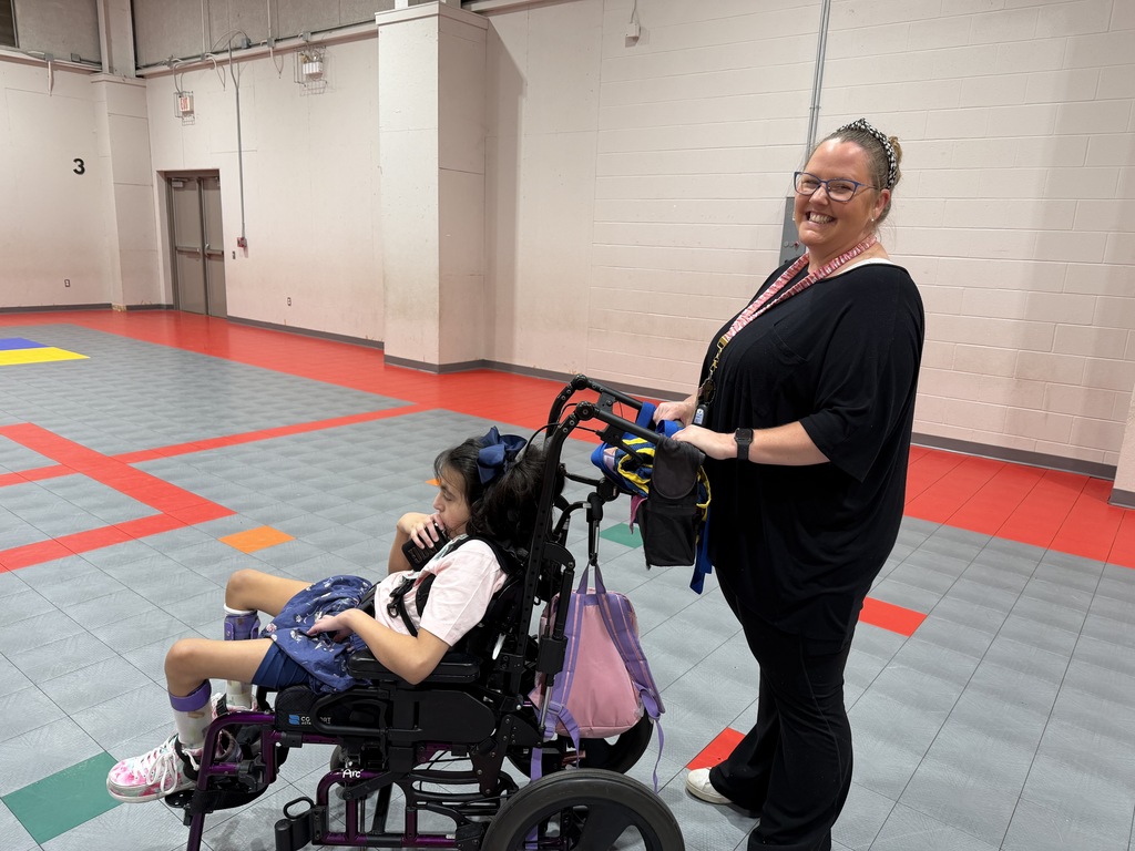 A woman assists a child in a wheelchair in a multicolored indoor room with a red floor.