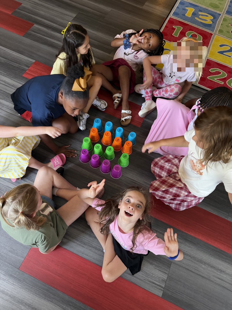 A group of children, sitting in a circle, playing with colorful cups on a red carpet.