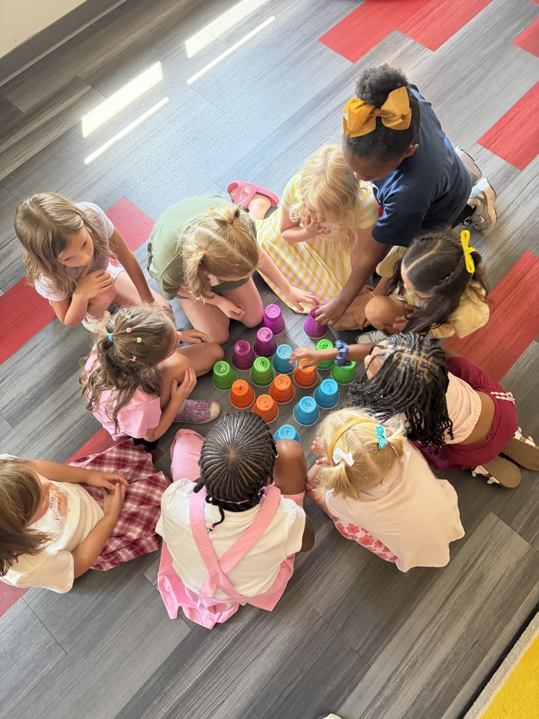 Group of children sitting in a circle, playing with colorful cups on a wooden floor.