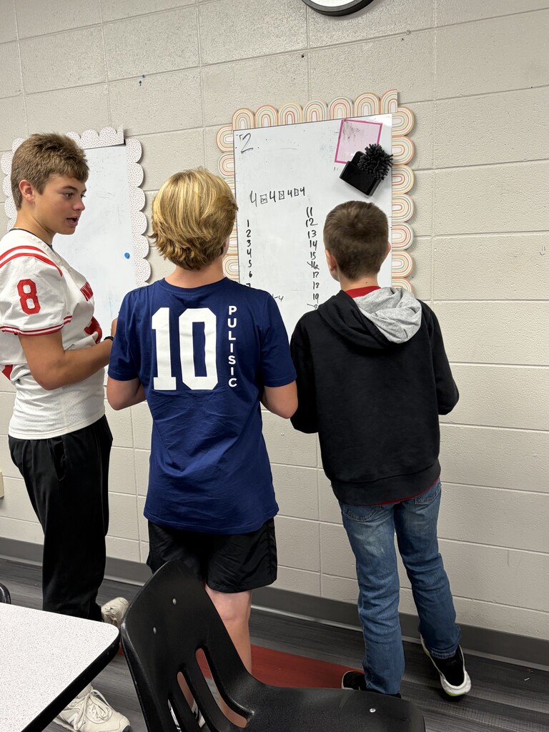 Three boys stand in a classroom with one wearing a football jersey with the number 10.