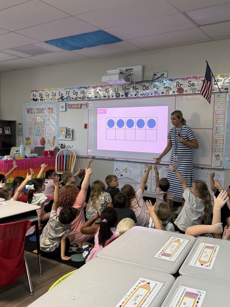 A classroom with a teacher and students. The teacher is presenting on a projector screen.