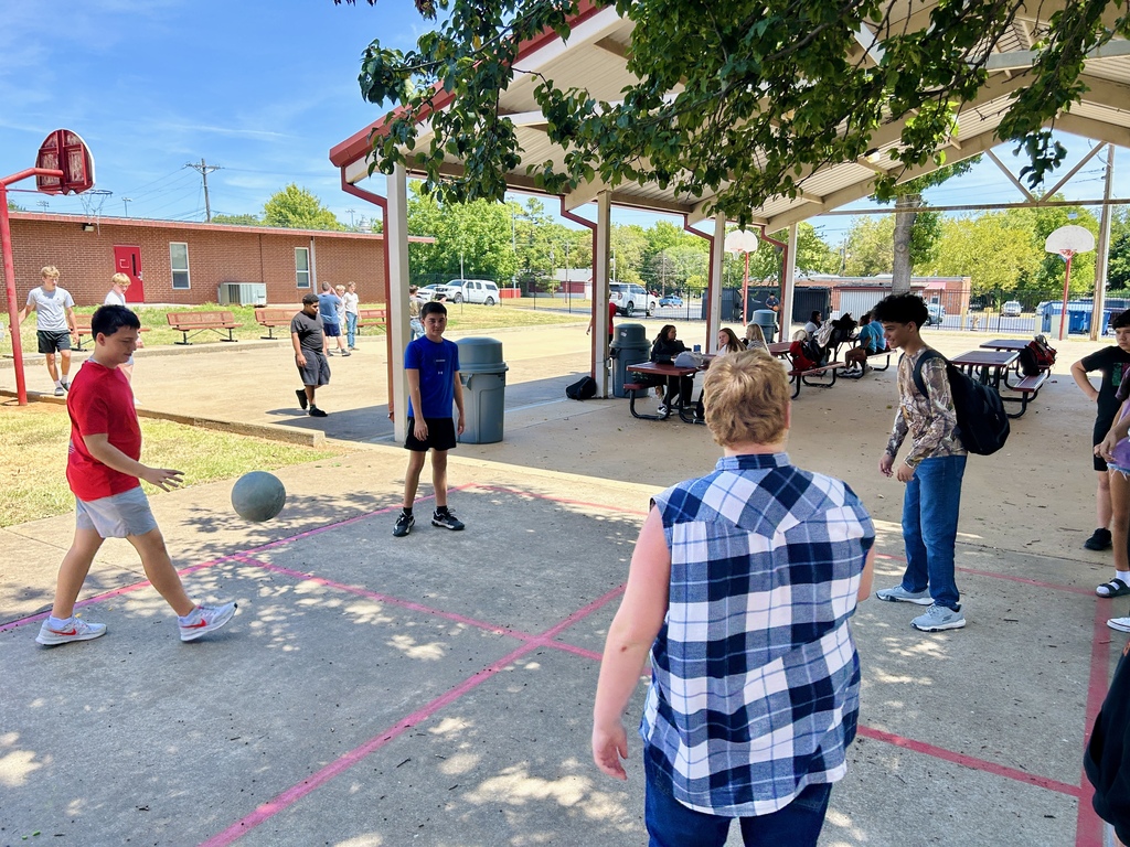 Four people play a game with a ball on a court with red lines.