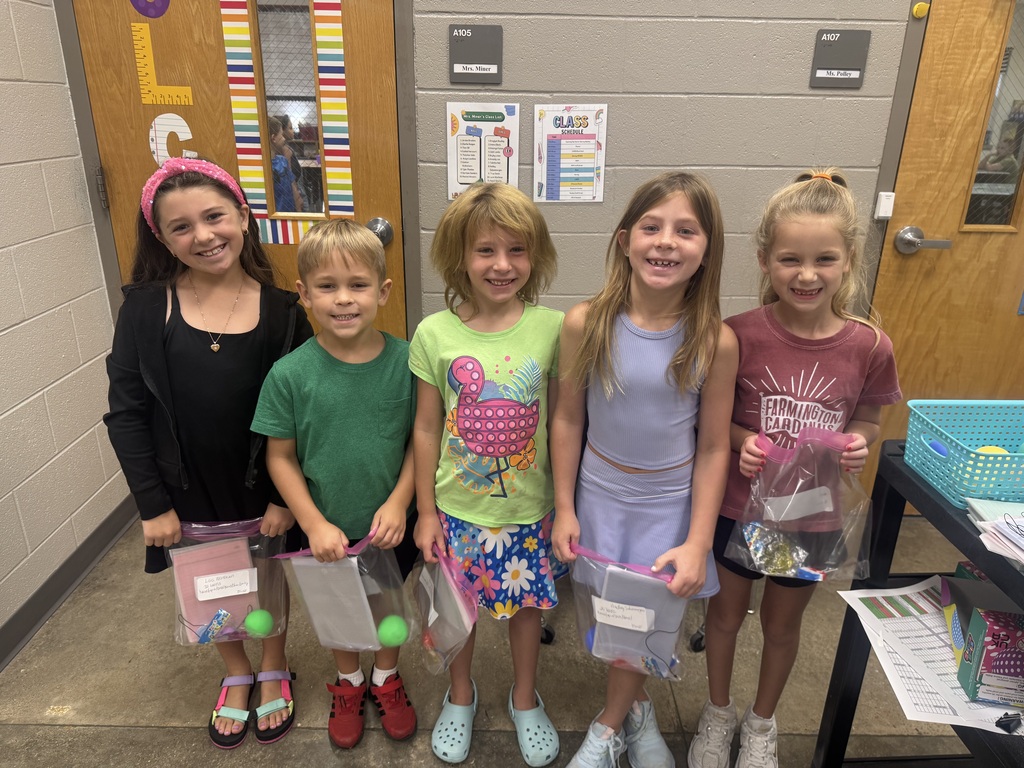 Six children standing in a room, smiling and holding items. Two doors are behind them.