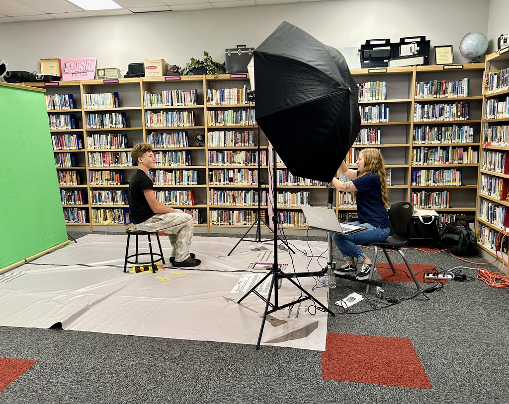 Two people in a library. One seated, the other with a laptop and an umbrella light.