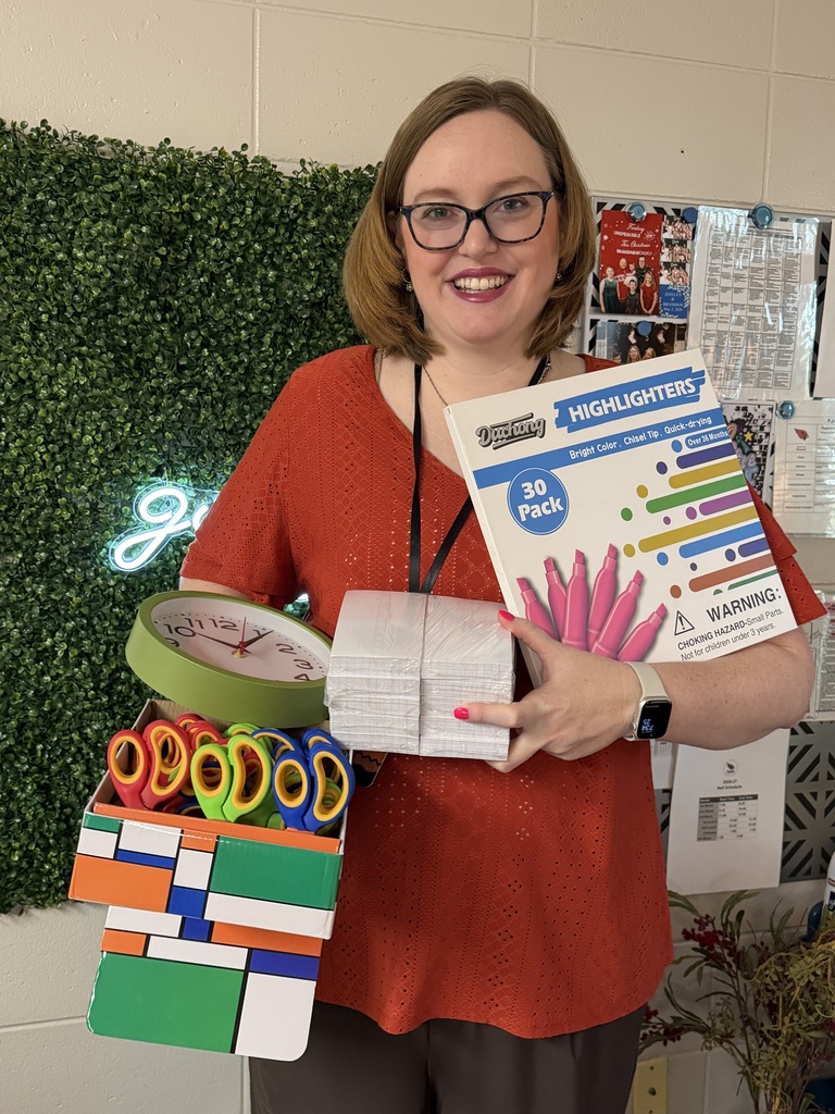 A woman in a red top holds a box of scissors, a colorful box, and a book.