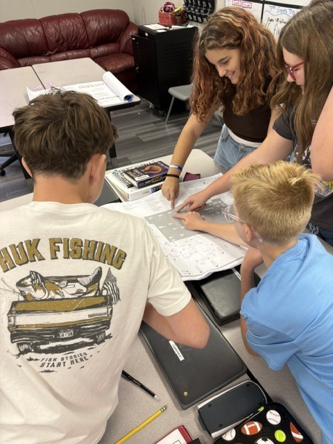 A group of students studying over a table. One student is pointing at a paper.
