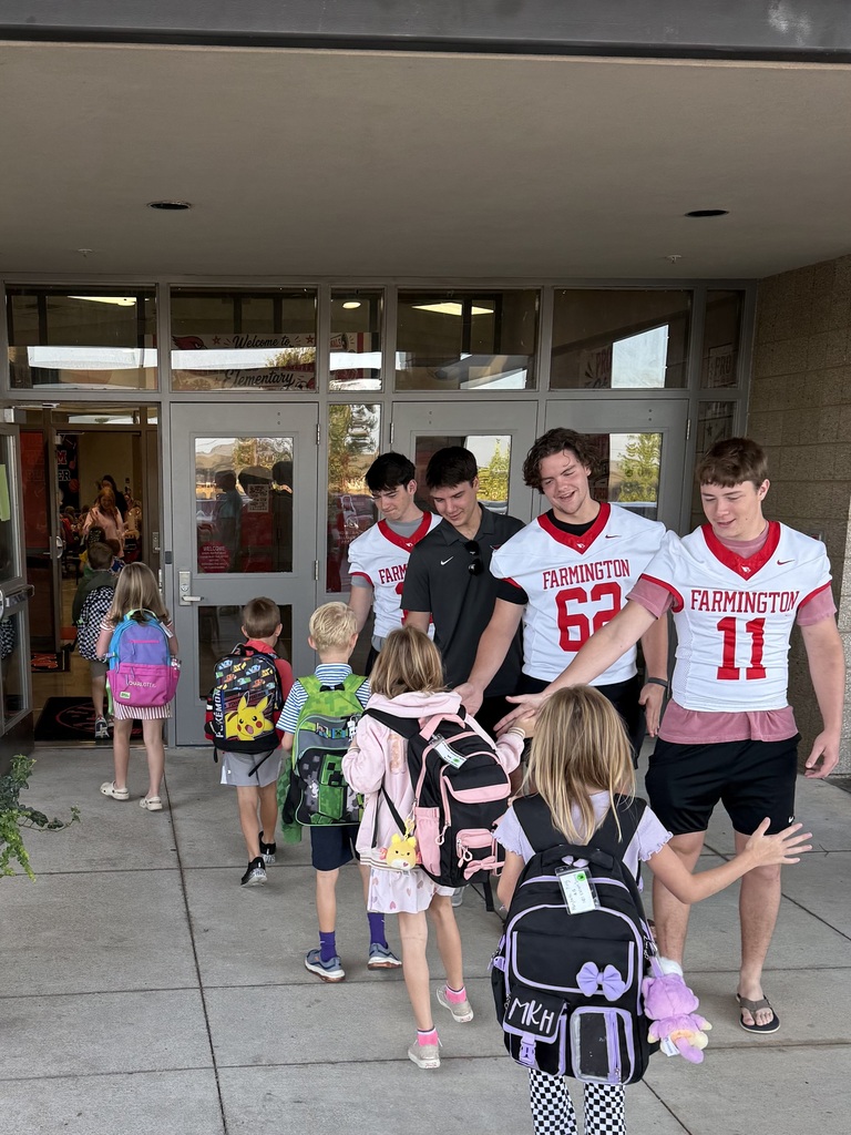 A group of children and adults with backpacks standing in front of a school entrance.