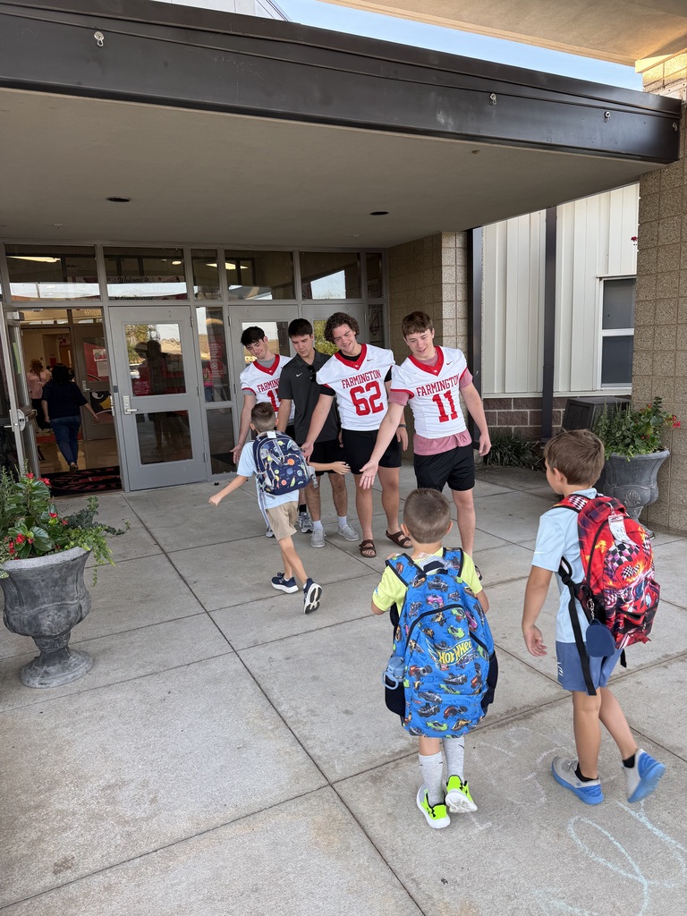 Children with backpacks and a group of kids in sports jerseys stand outside a building.