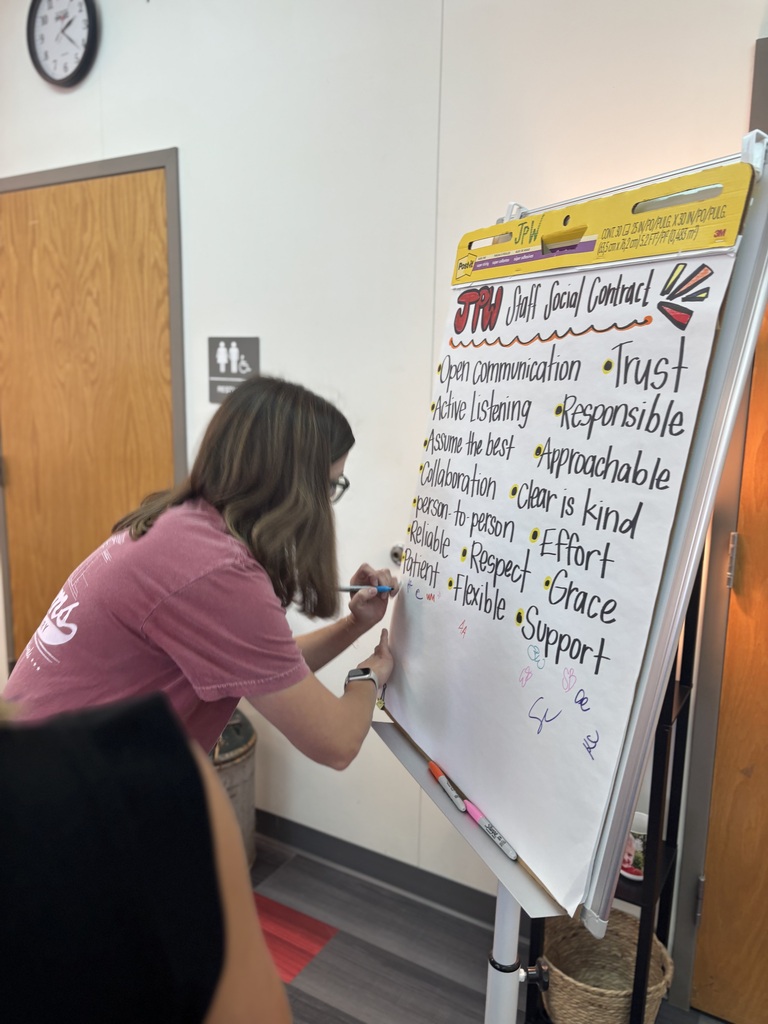 A person in a pink shirt writes on a whiteboard with words such as "trust," "effort," and "grace."